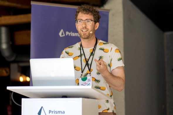 Me smiling and speaking at a conference podium, wearing a pineapples-on-white t-shirt, gesturing with one hand